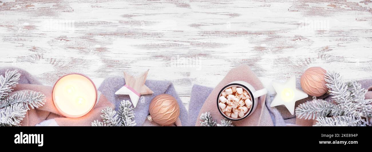Cozy Christmas or winter bottom border with grey and dusty pink sweater, candle, hot chocolate, snowy branches and decor. Top down view over a rustic Stock Photo