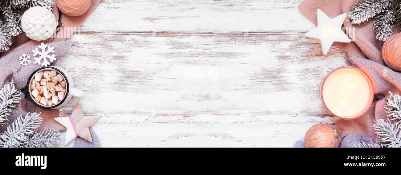 Cozy Christmas or winter double border with grey and dusty pink sweater, candle, hot chocolate, snowy branches and decor. Top view over a rustic white Stock Photo
