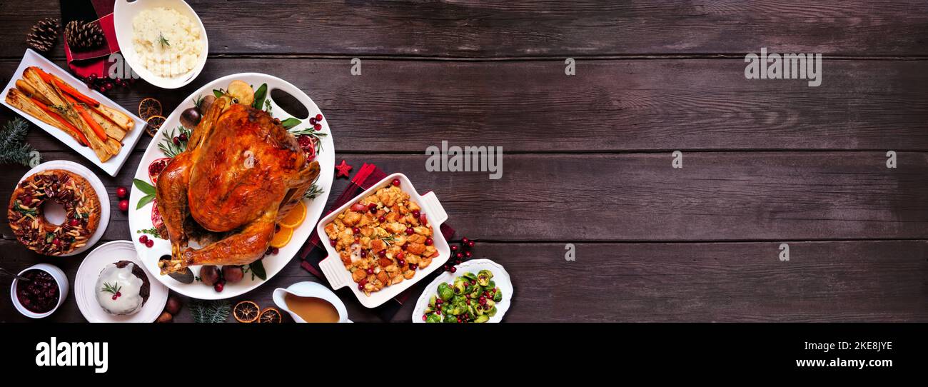 Traditional Christmas turkey dinner. Above view corner border on a dark wood banner background. Turkey, potatoes and sides, dressing, fruit cake and p Stock Photo