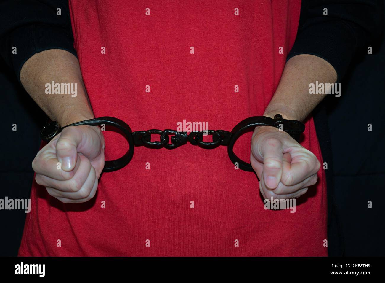 Photo of a pair of women's hands with iron shackles in front of a red shirt. Stock Photo