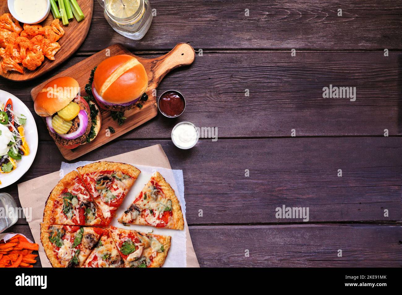 Healthy plant based fast food side border. Above view over a dark wood background. Table scene with cauliflower crust pizza, bean burgers and vegetari Stock Photo