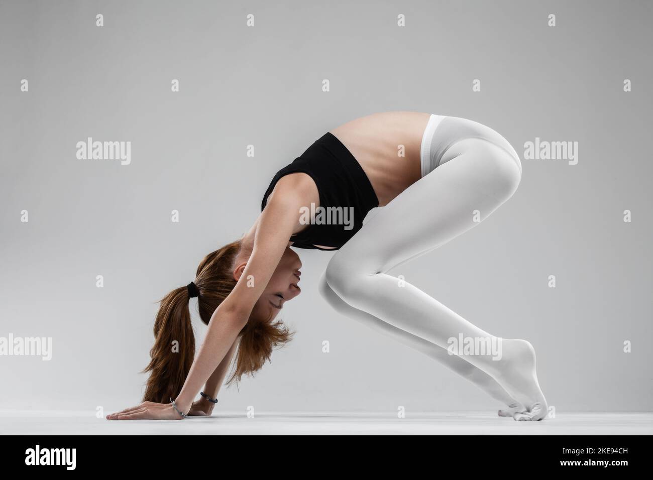 Fit ballerina girl stretching and practicing yoga poses against gray ...