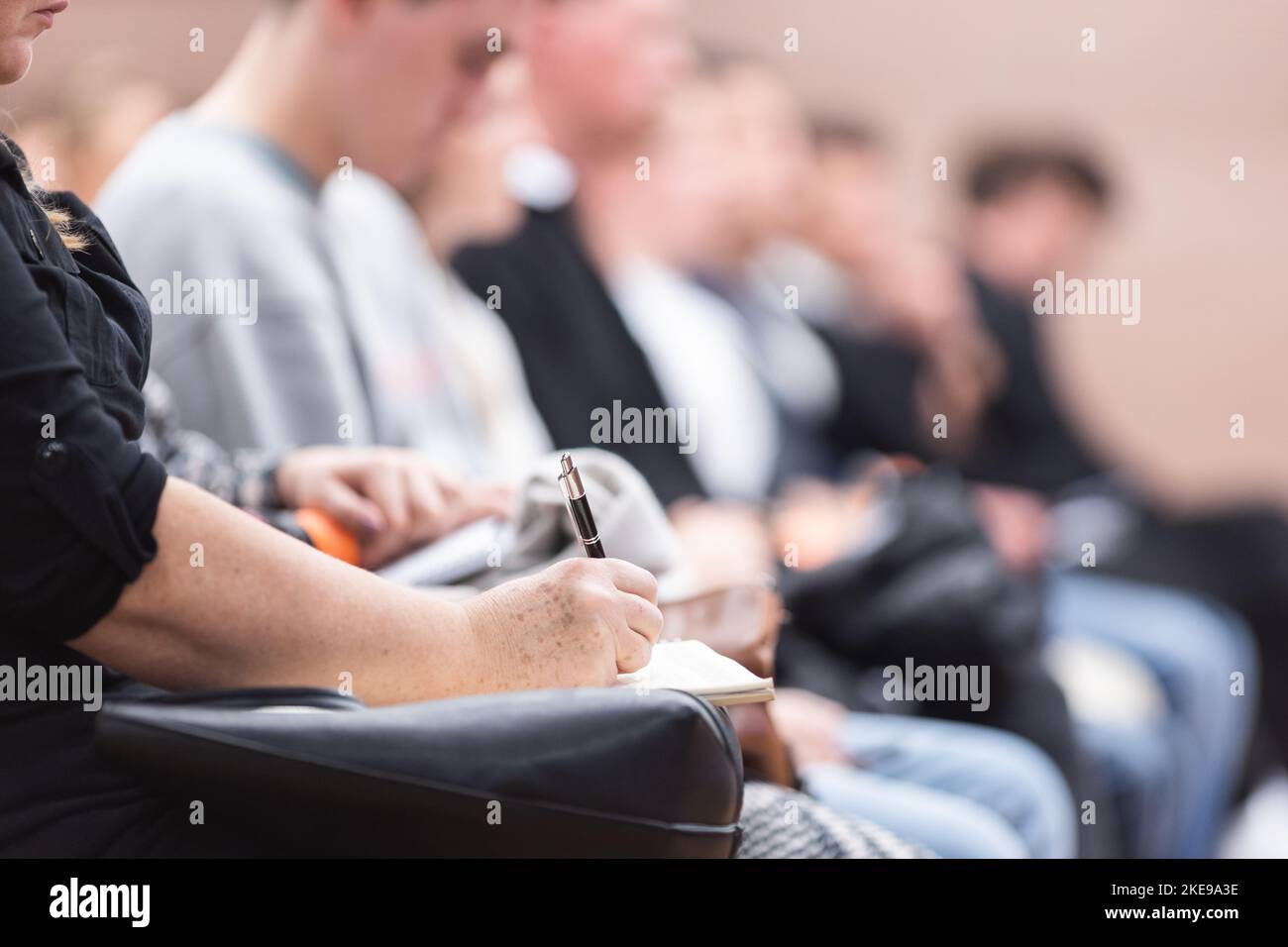 Female hands holding pen and notebook, making notes at conference lecture. Event participants in conference hall Stock Photo