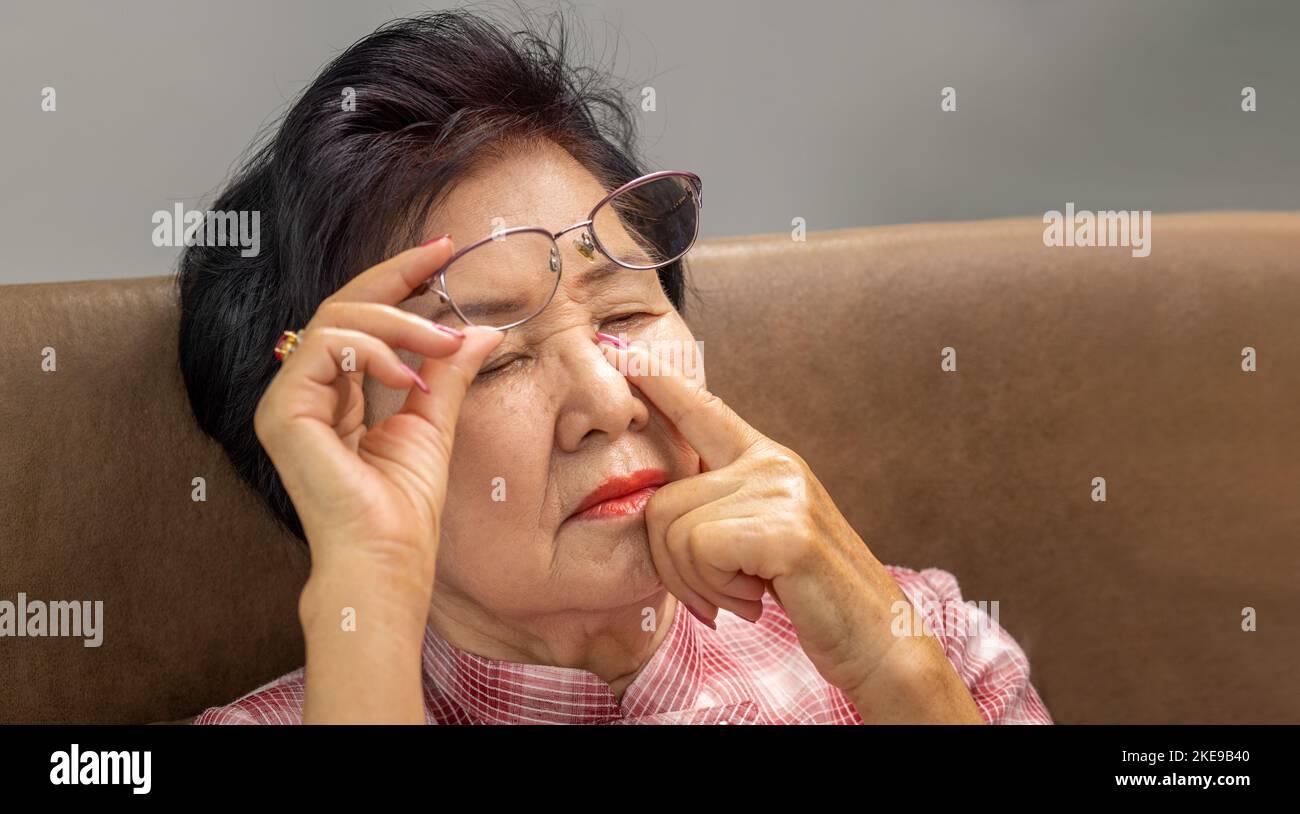 Asian senior older woman taking off glasses, suffering from dry eyes syndrome Stock Photo