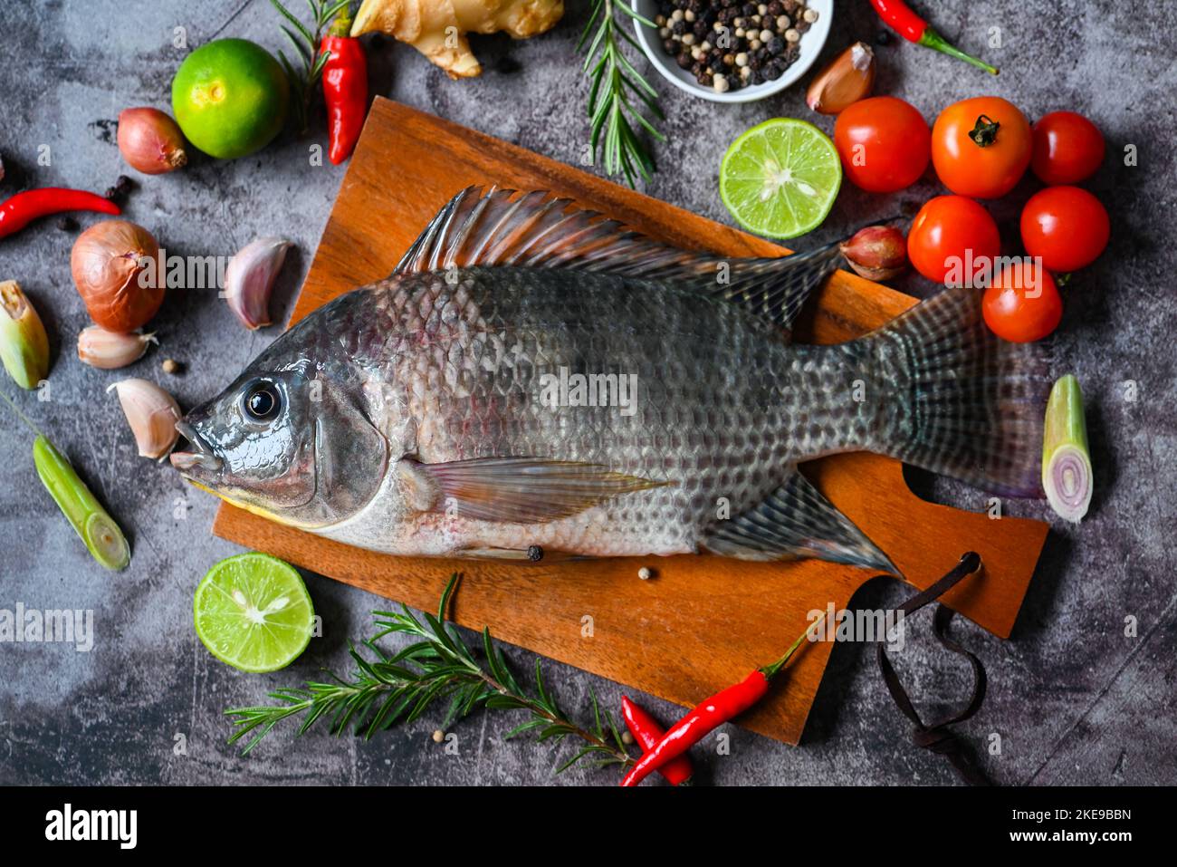 Tilapia with spice rosemary tomato lemon lime ginger garlic pepper chili on dark background