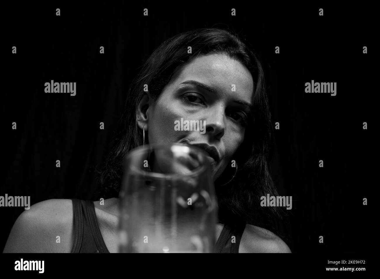 A Caucasian young woman looking at camera behind glass of beer in black