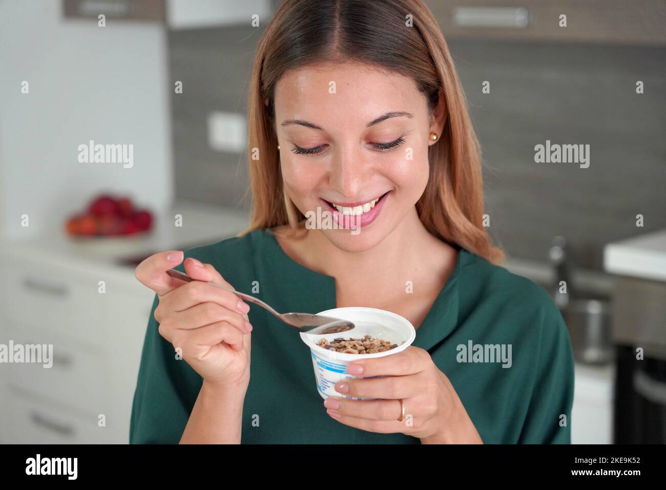 Sweet woman holds bowl of Greek yogurt with muesli in the kitchen Stock