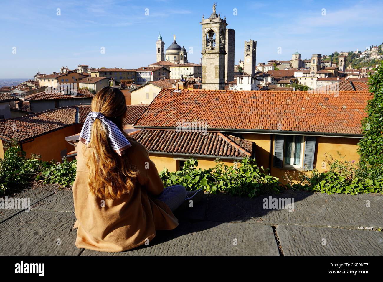 Tourism in Bergamo, Italy. Back view of girl sitting on wall in upper city enjoying cityscape of Bergamo, Lombardy, Italy. Stock Photo