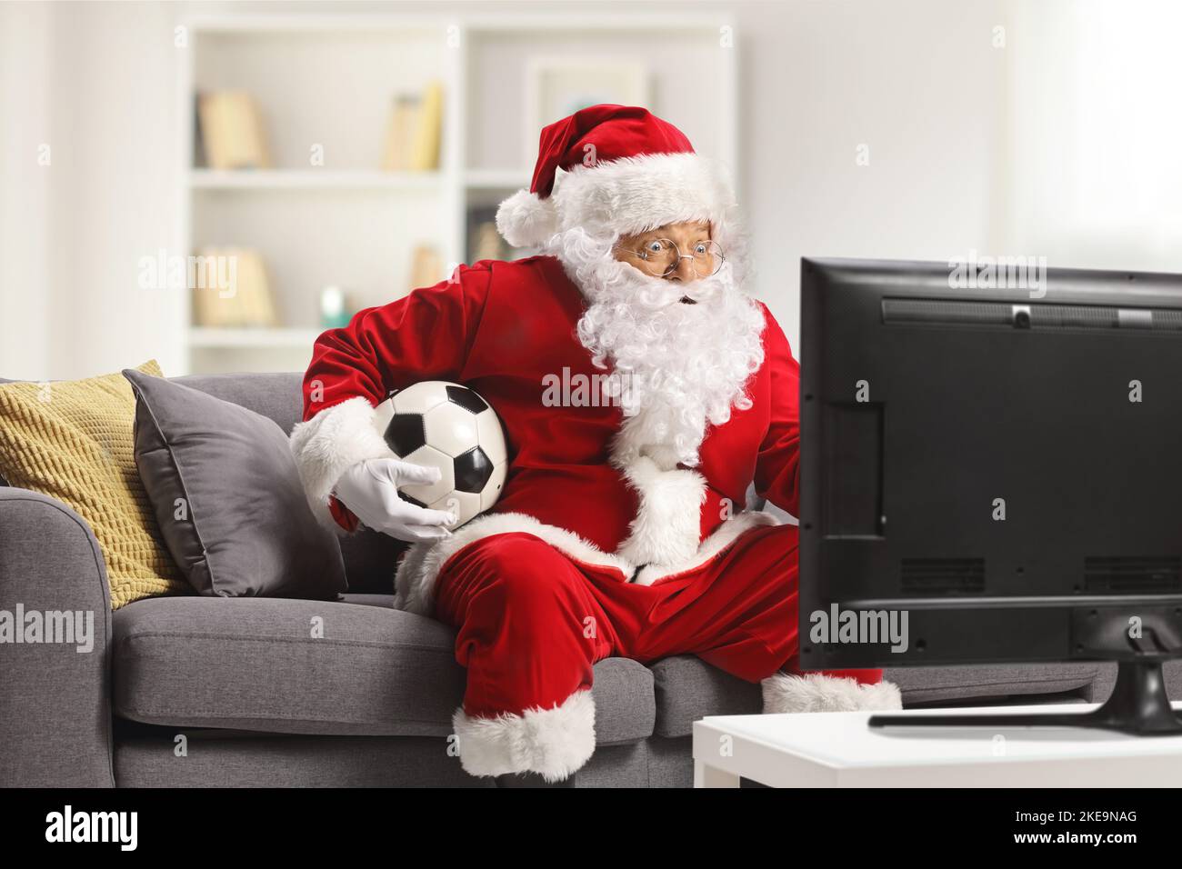 Santa claus sitting on a sofa and watching football on tv in a living