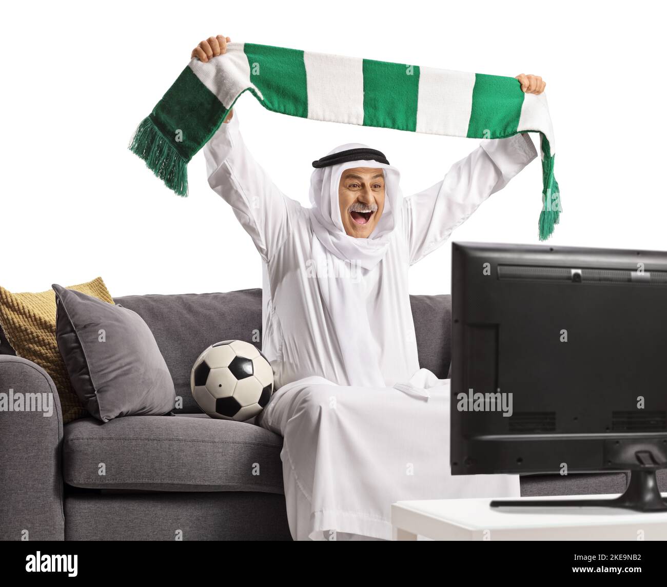 Happy arab man cheering with a scarf watching football and sitting on a sofa isolated on white background Stock Photo