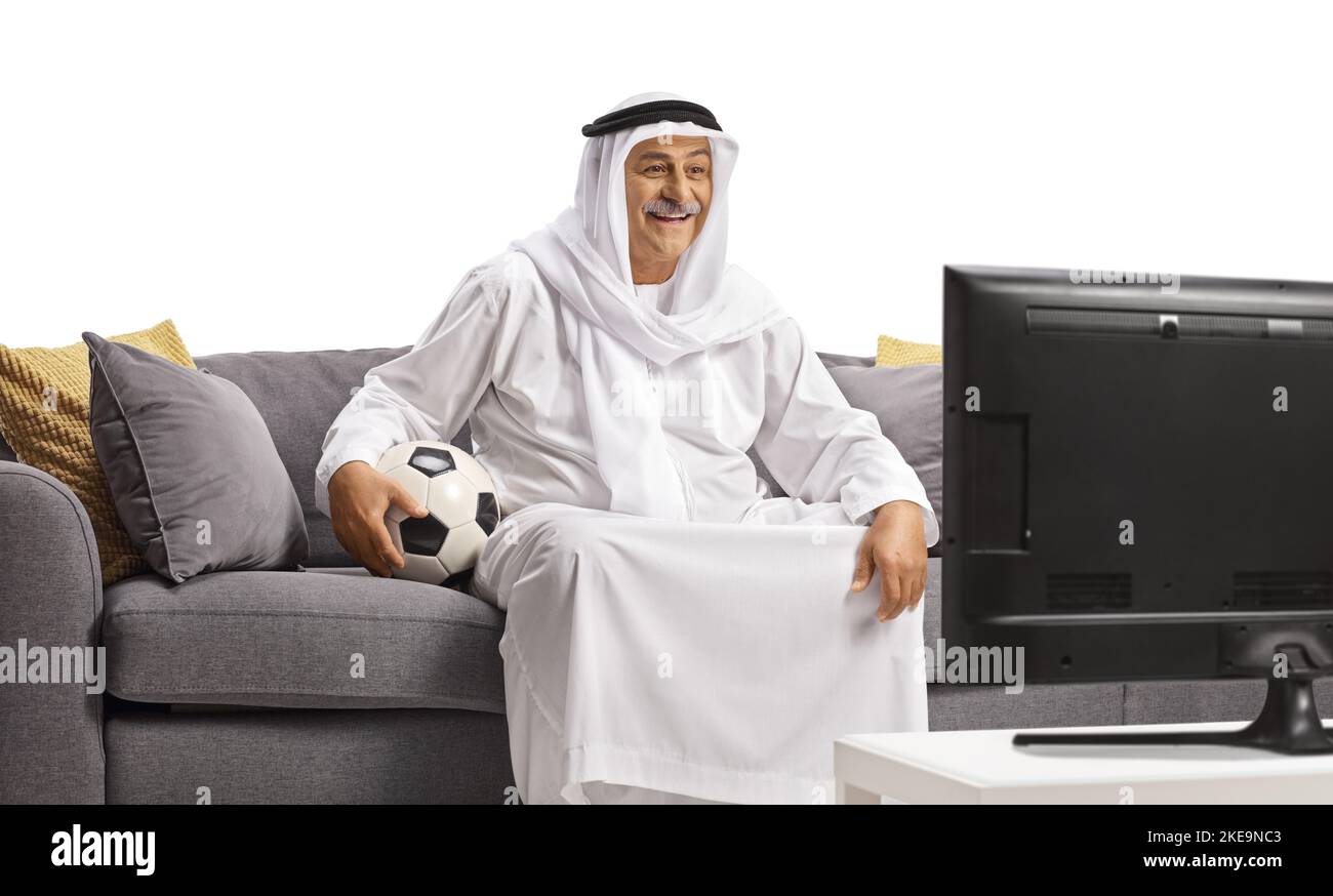 Arab man in a robe holding a ball and watching football on tv isolated on white background Stock Photo
