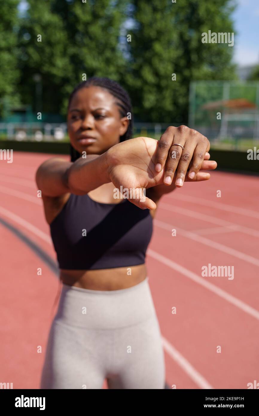 African American female stretches hands warming up before intensive workout on sunny summer day Stock Photo