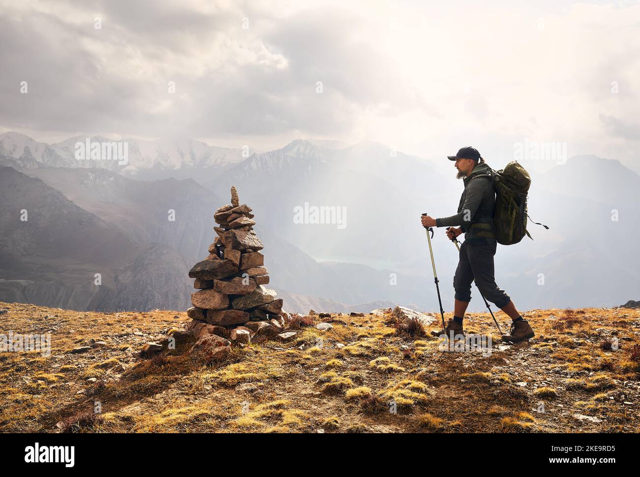 Man Hiker tourist with big backpack in silhouette on the hill against cloudy sky in the mountain valley. Outdoor and trekking concept. Stock Photo