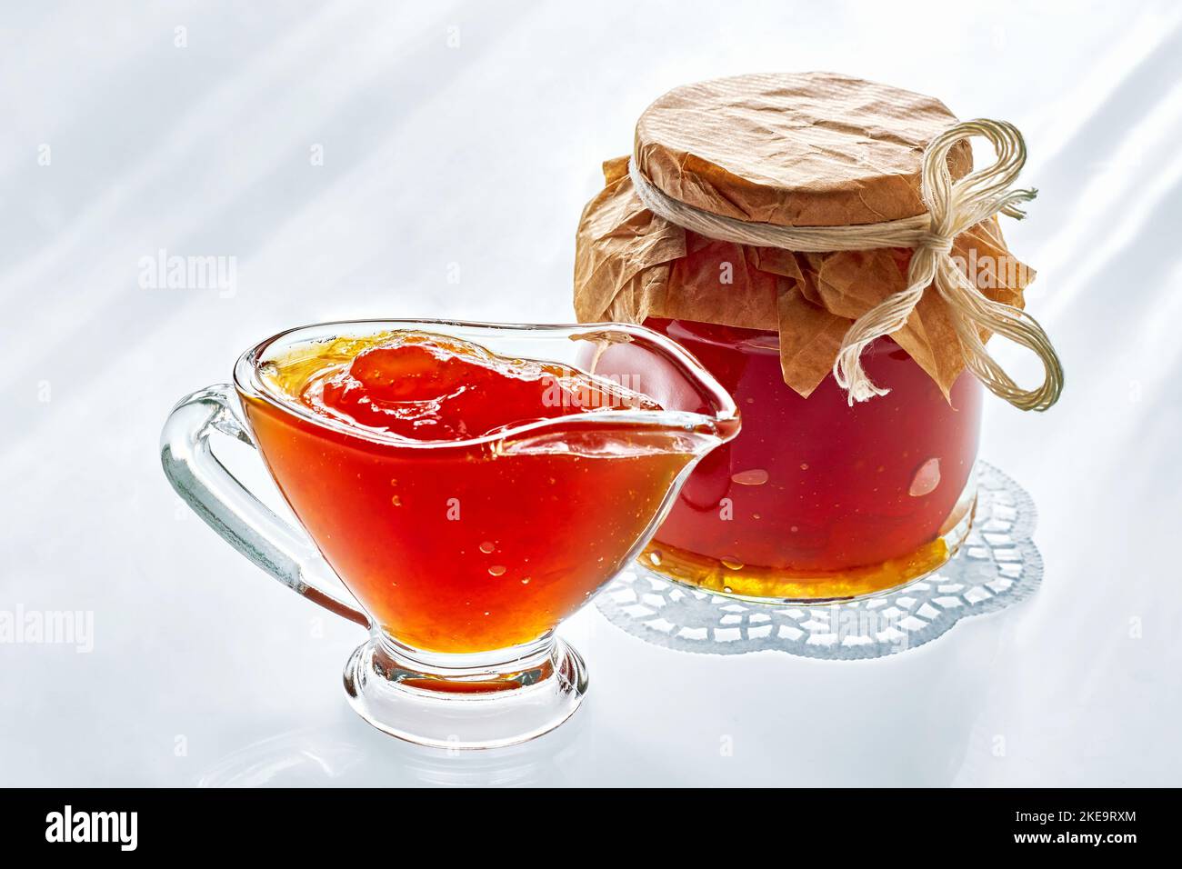 Sweet orange color fruit jam in a glass gravy boat and in a jar on a light morning background Stock Photo