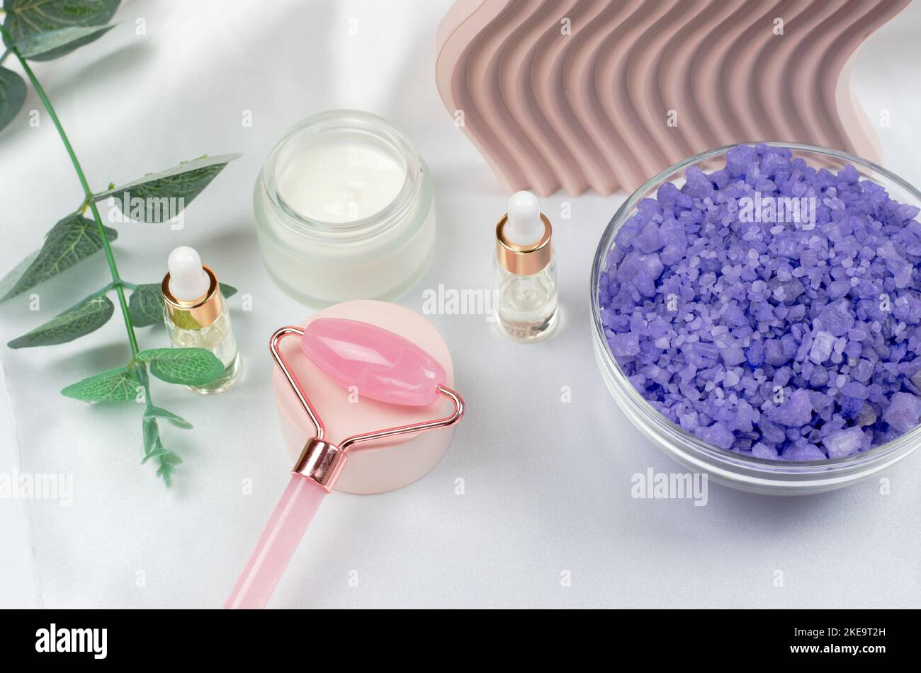 Rose quartz facial roller with face oil, face moisturizer and lavender sea salt on a white table background. Facial massage kit for lifting massage th Stock Photo