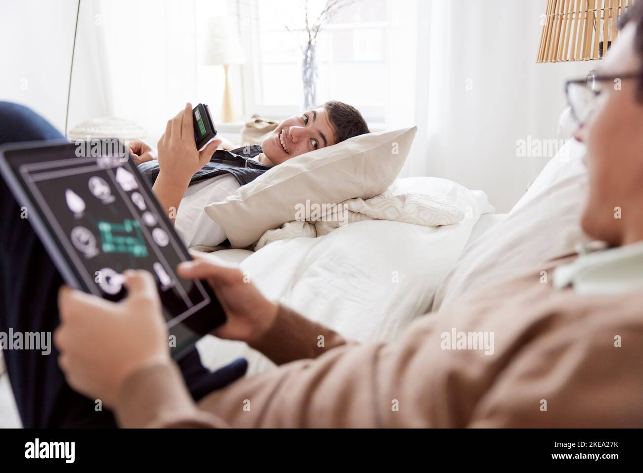 Brothers lying on bed and using phone and tablet Stock Photo