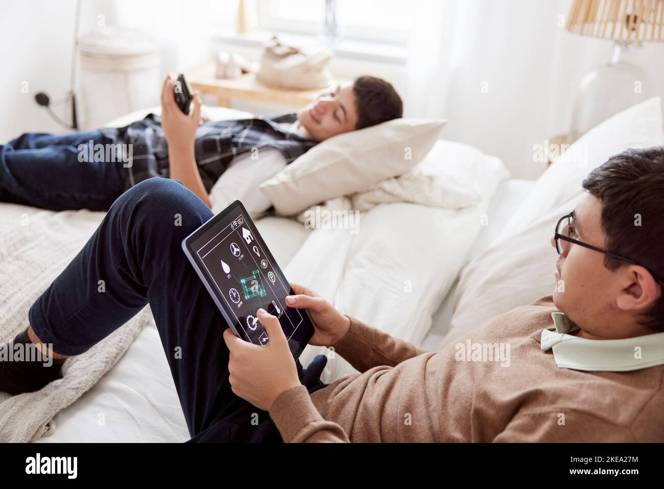 Brothers lying on bed and using phone and tablet Stock Photo