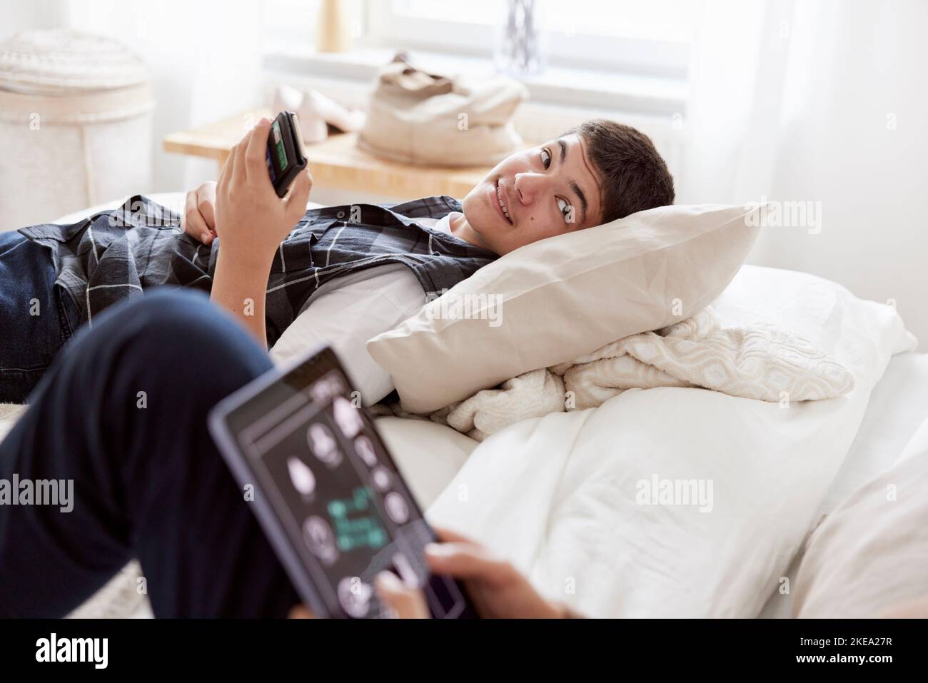 Brothers lying on bed and using phone and tablet Stock Photo
