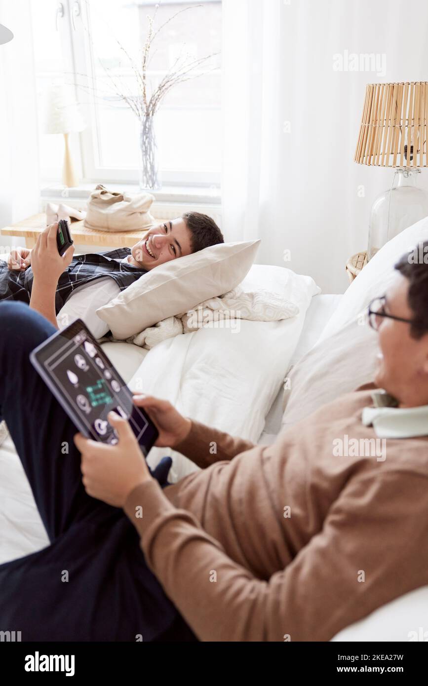 Brothers lying on bed and using phone and tablet Stock Photo