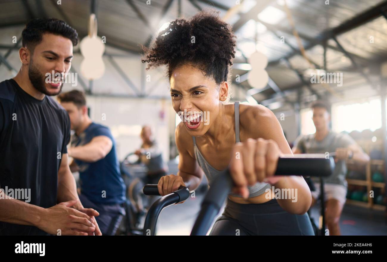 Gym, fitness and woman on bike with personal trainer for motivation, support and power workout, cheering and clapping hands. Coach, black woman and Stock Photo
