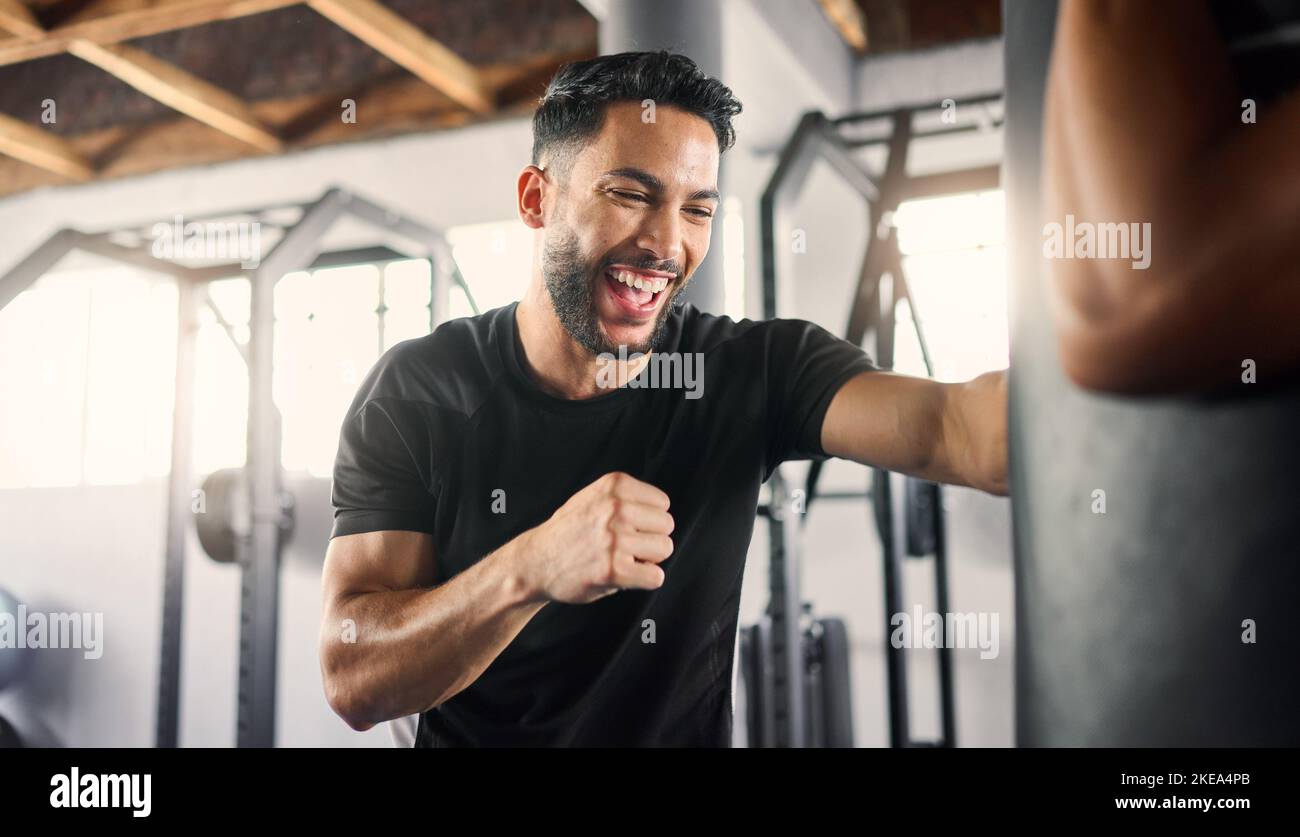 Boxing gym, fitness and happy athlete boxer punching a training bag in a martial arts studio or club. Happiness of a man in a fight workout and sport Stock Photo