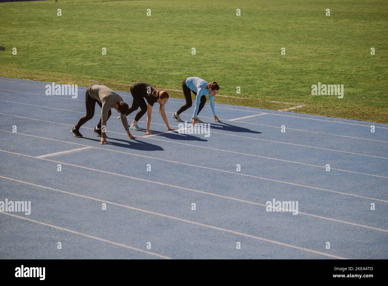 Two girls and one boy are preparing for 100m running race Stock Photo