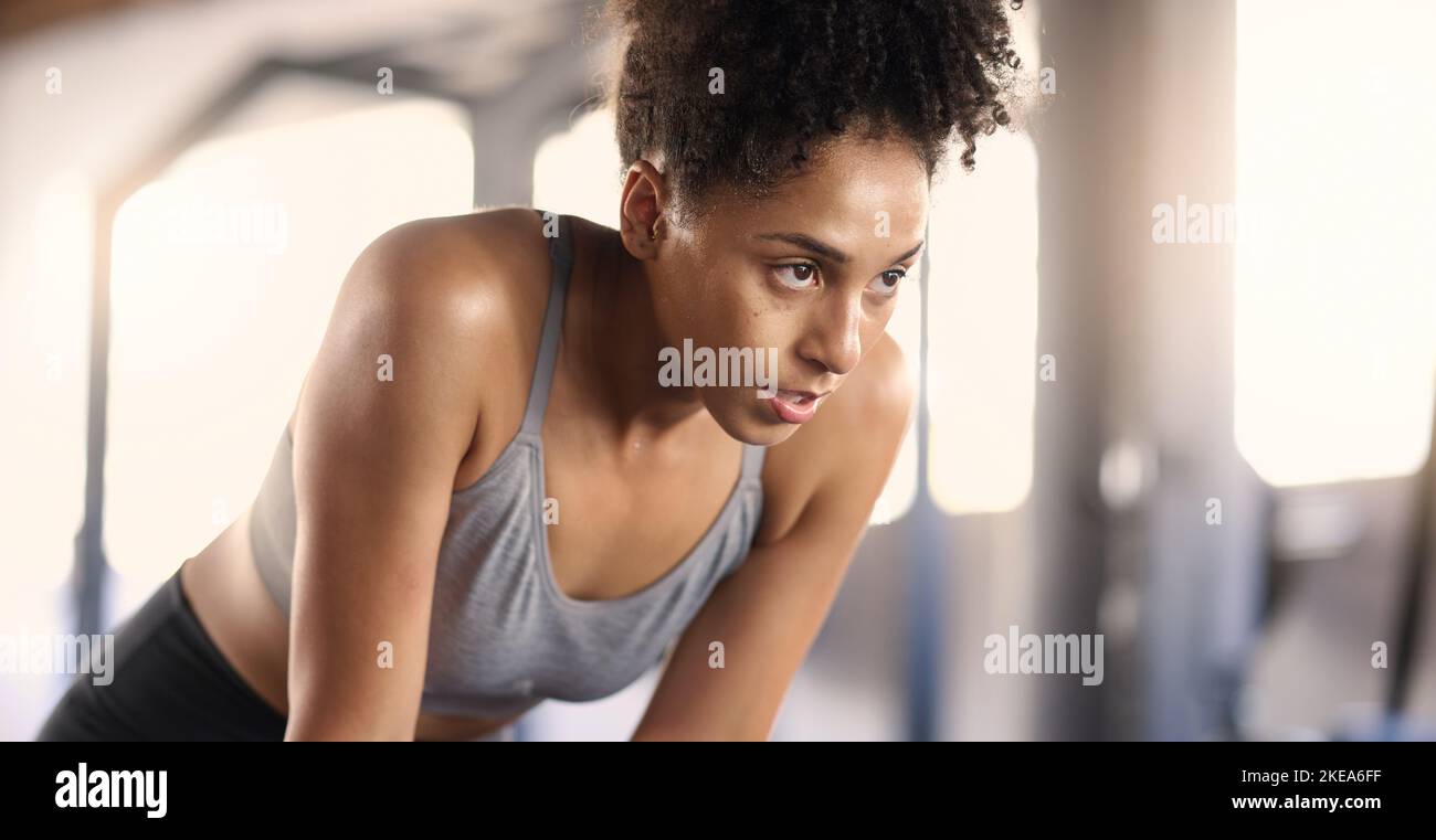Gym, training and tired black woman breathing after exercise, workout and sports fitness. Woman in a health and wellness club breathe and relax after Stock Photo