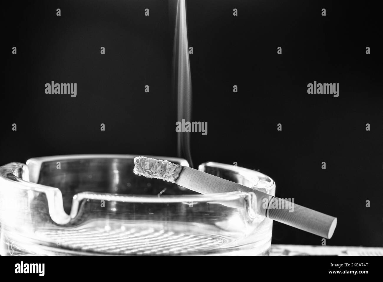 Burning cigarette smoke in glass ashtray dark background copy space