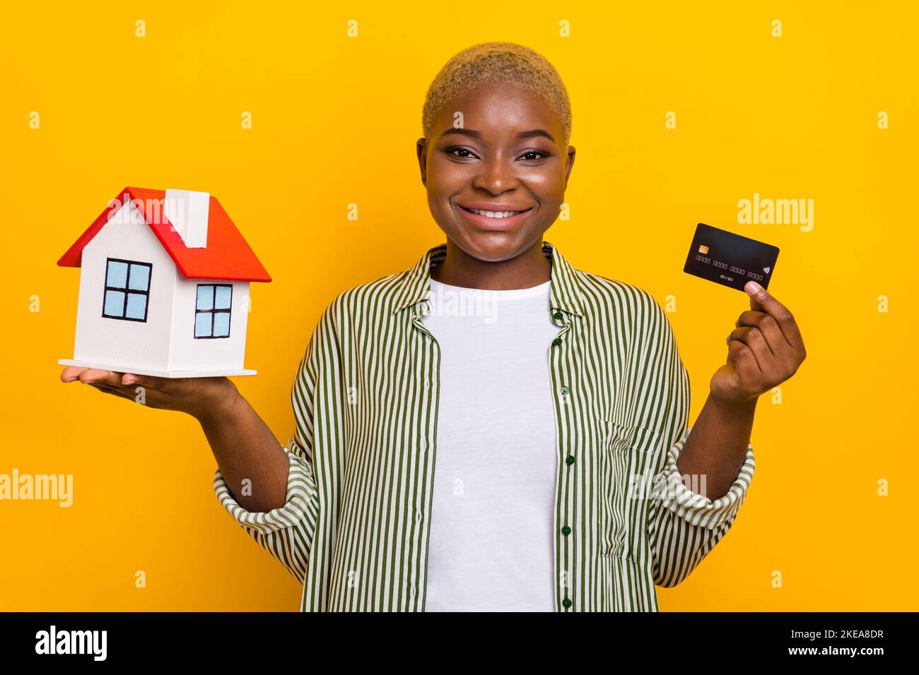 Portrait of attractive cheerful girl hands hold show small house debit card isolated on yellow color background Stock Photo