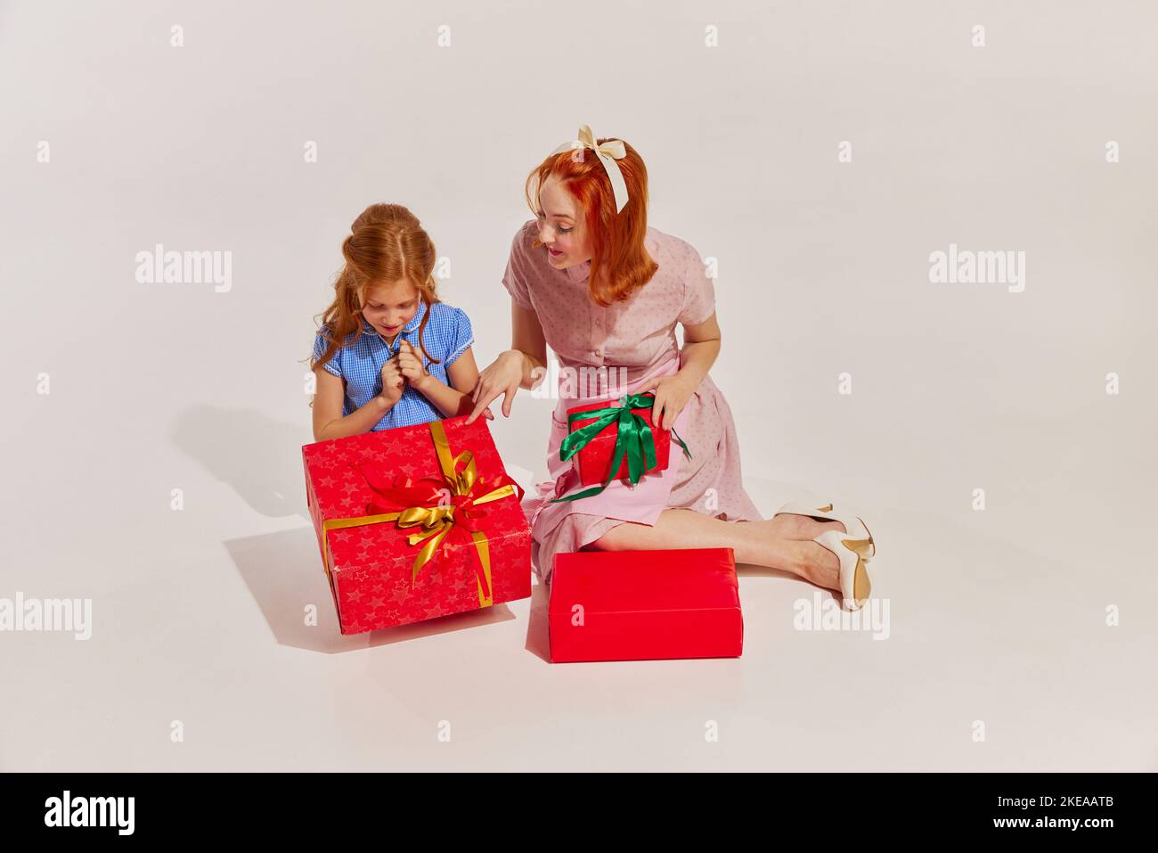 Portrait of beautiful woman and little girl, mother and daughter wrapping presents isolated over grey background Stock Photo