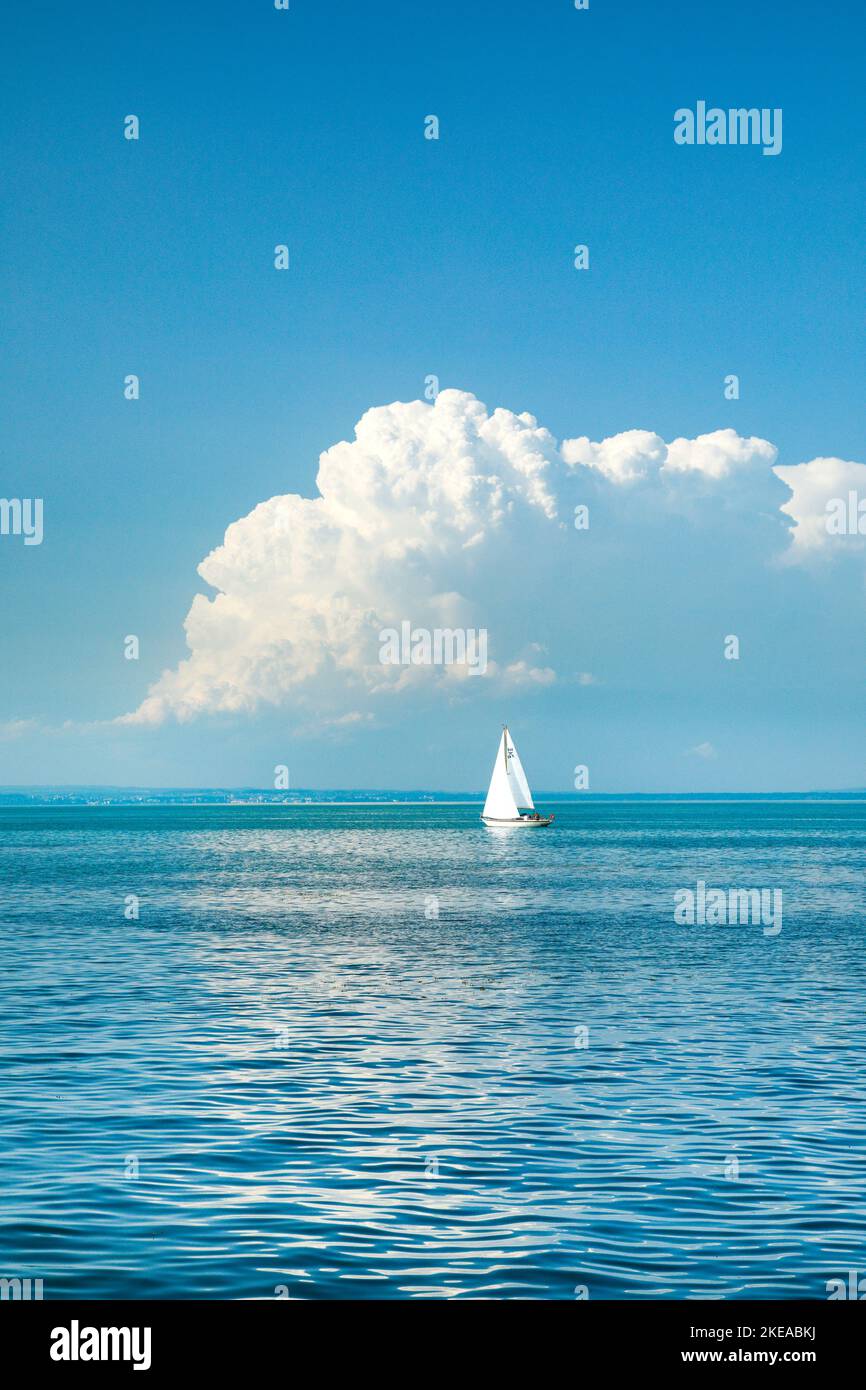 Weisses Segelboot auf dem türkisblauen Wasser des Bodensee mit tiefstehender, grossen Quellwolke im Hintergurnd, Kanton Thurgau, Schweiz Stock Photo