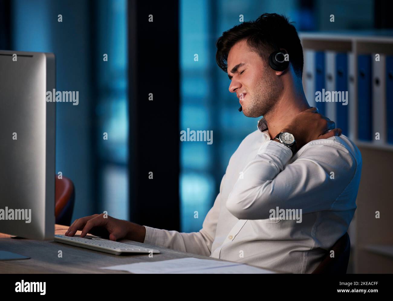 Call center, neck pain and business man at night with burnout, stress and fatigue at office desktop computer consulting. Telemarketing or salesman Stock Photo