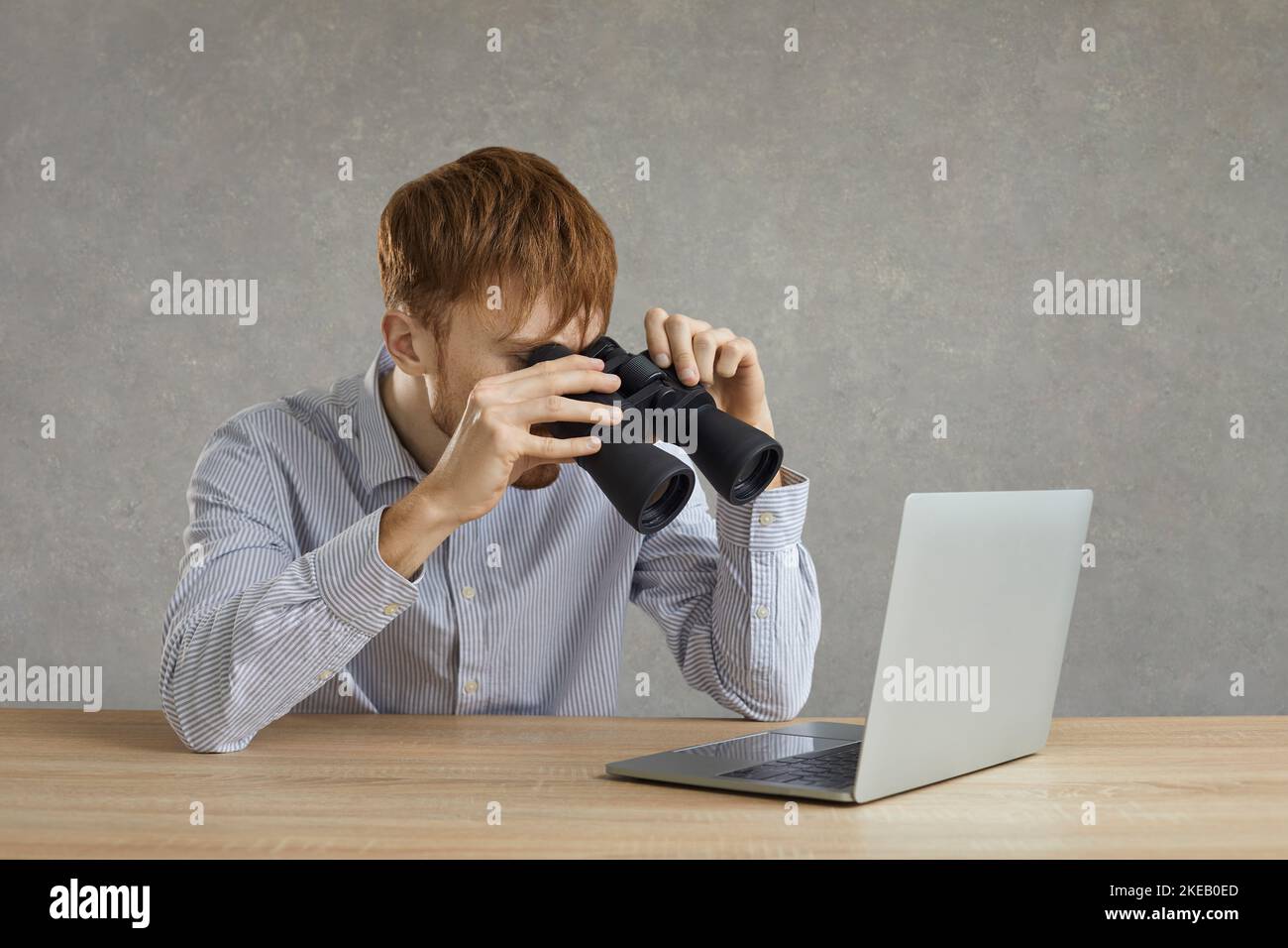 Young man office employee looking at laptop screen through binocular studio shot Stock Photo