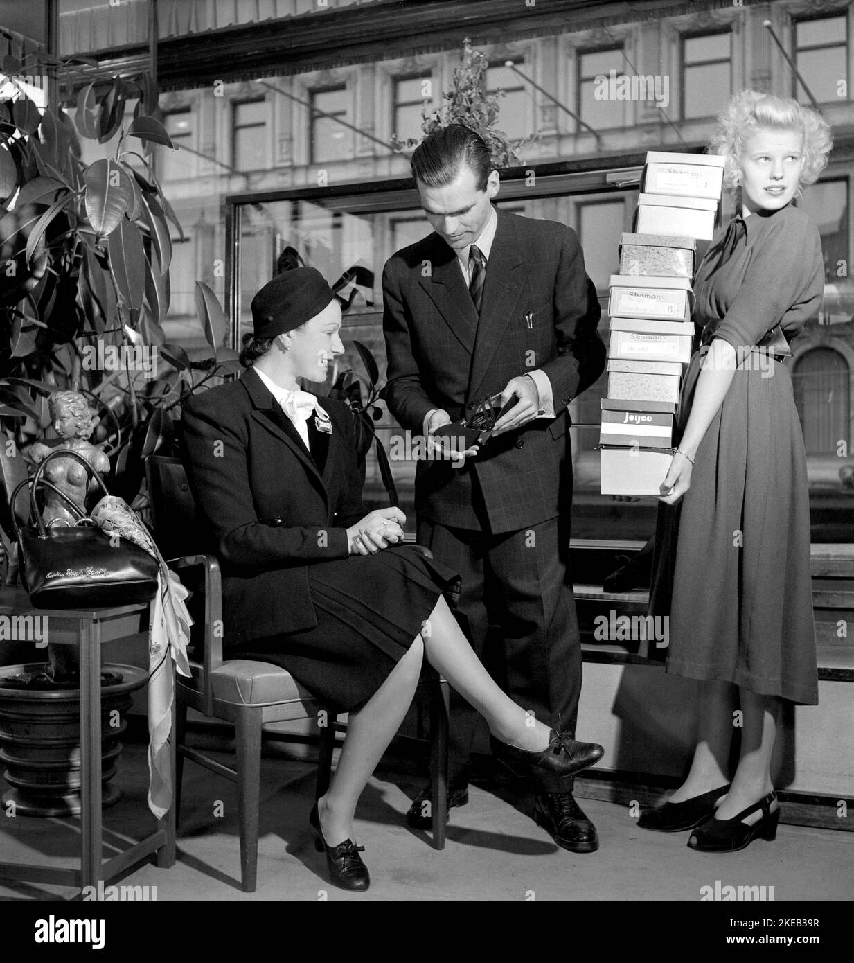 Shoe store in the 1940s. A woman in the shoestore on Hamngatan Stockholm 1948. She is being serviced perfectly with a sales clerk showing a fashionable shoe model, and a female assistant with boxes of shoes ready to be tried on. Sweden 1948. Conard ref 957 Stock Photo