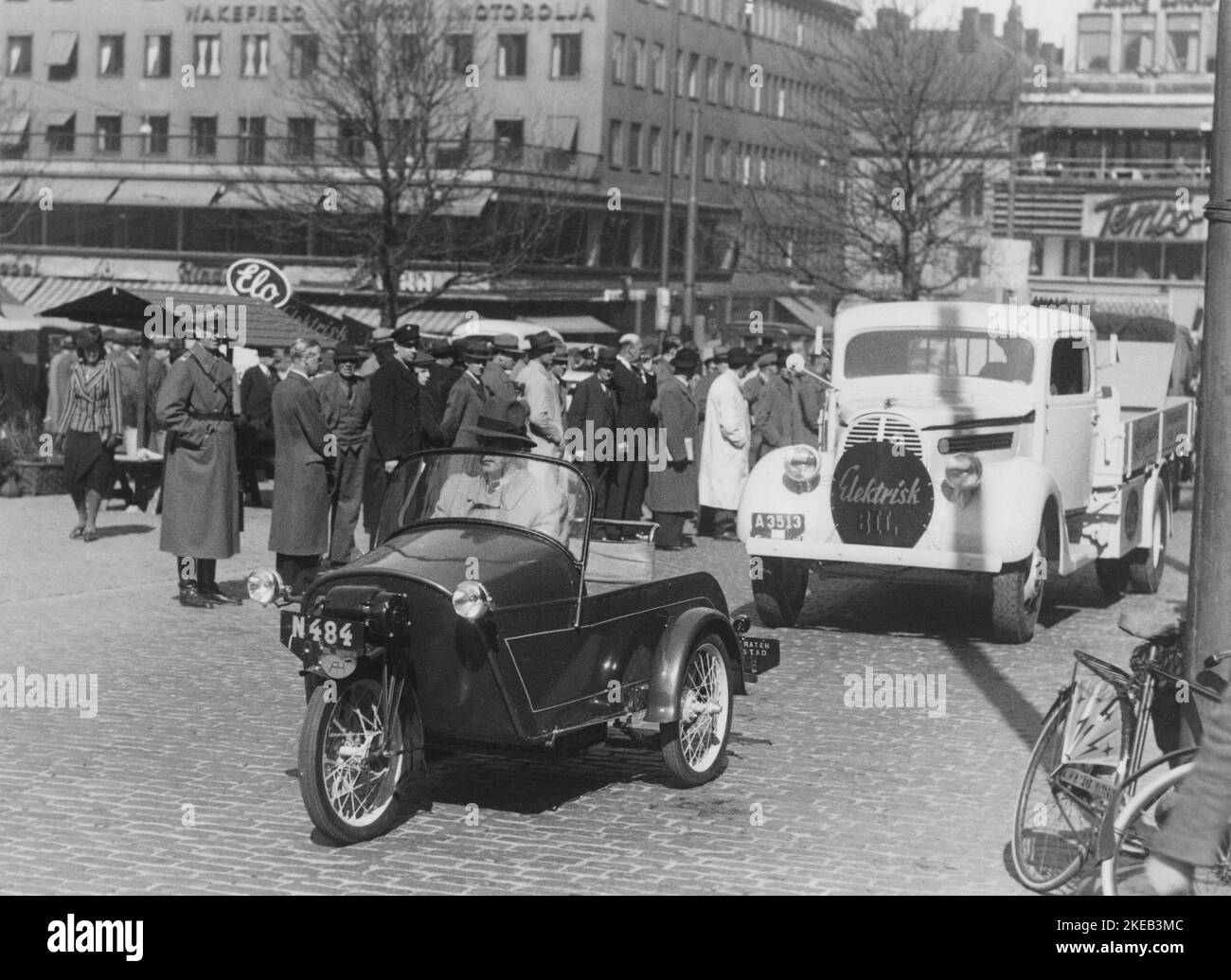 Cars in the 1940s. During the time of  world war II electric cars began to interest people. Diesel and petrol were rationed and new ways of fueling cars and vehicles was experimented on. Pictured two electric powered vehicles being showed for the public in Stockholm Sweden. In front a three-wheeled electric vehicle with a man driving it. Behind a electric powered lorry truck. Stockholm Sweden 1940s. Stock Photo