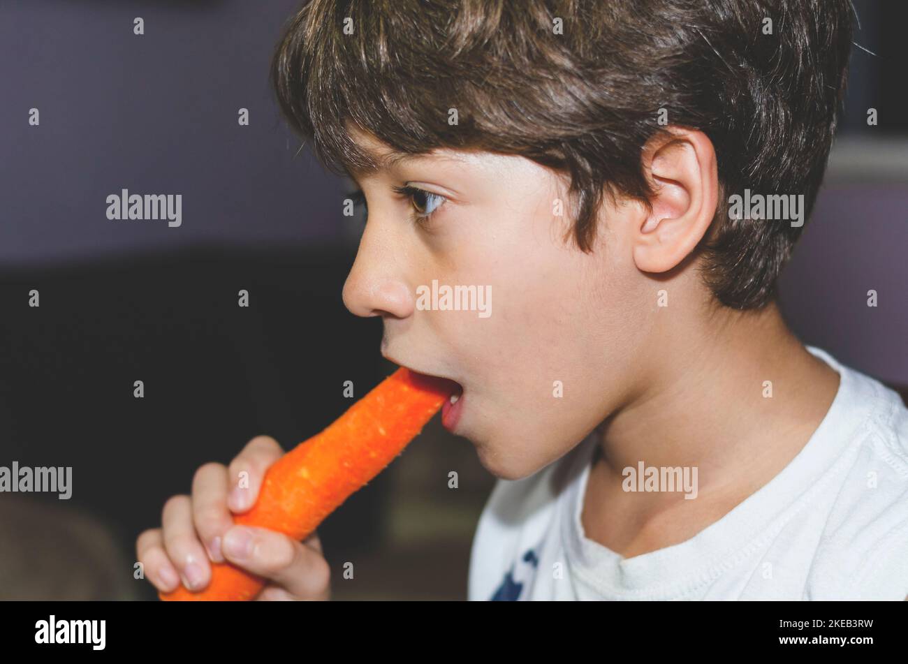 Happy little boy eating a fresh carrot and having fun. Healthy vegetarian food. At home. Salvador, Brazil. Stock Photo