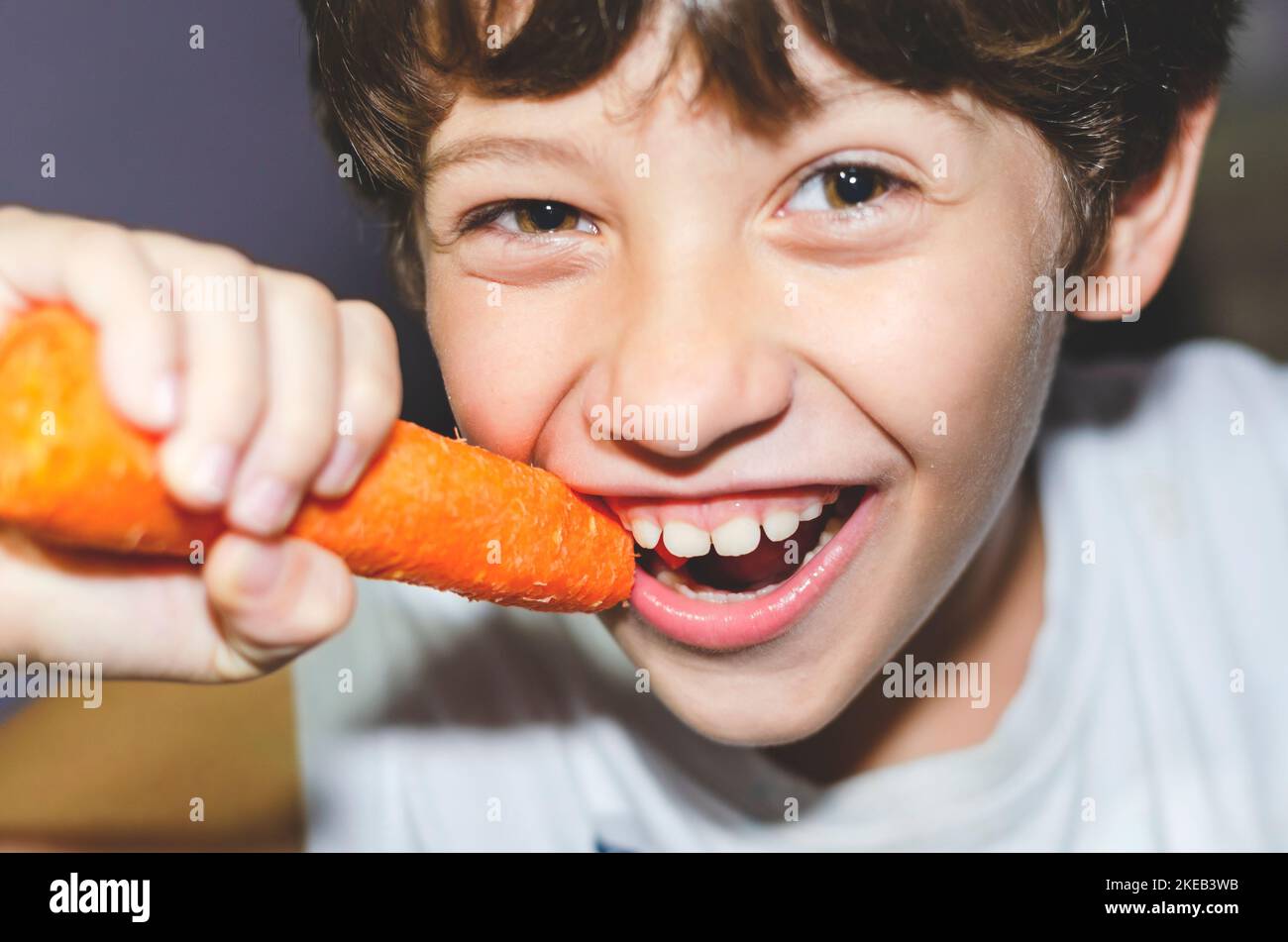 Happy little boy eating a fresh carrot and having fun. Healthy vegetarian food. At home. Salvador, Brazil. Stock Photo