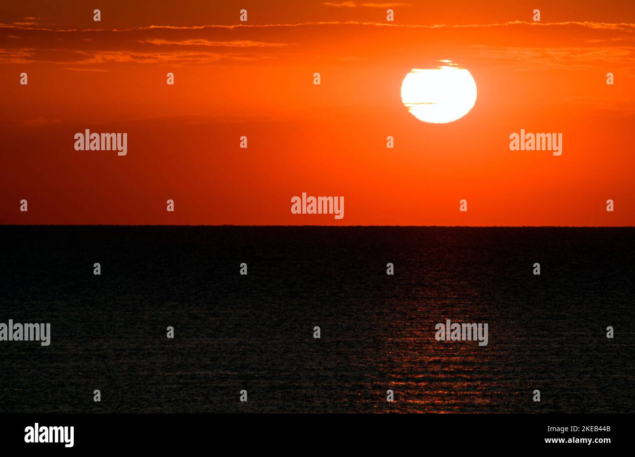A spectacular sunrise over the sea, the sun rising from beyond the horizon line in a beautiful red sky. Stock Photo