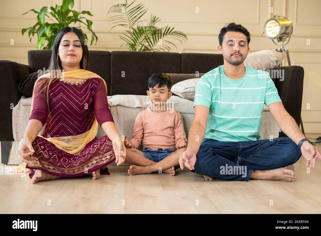 young couple with kid meditating on floor at home - concept of mindfulness, family rituals and spirituality. Stock Photo