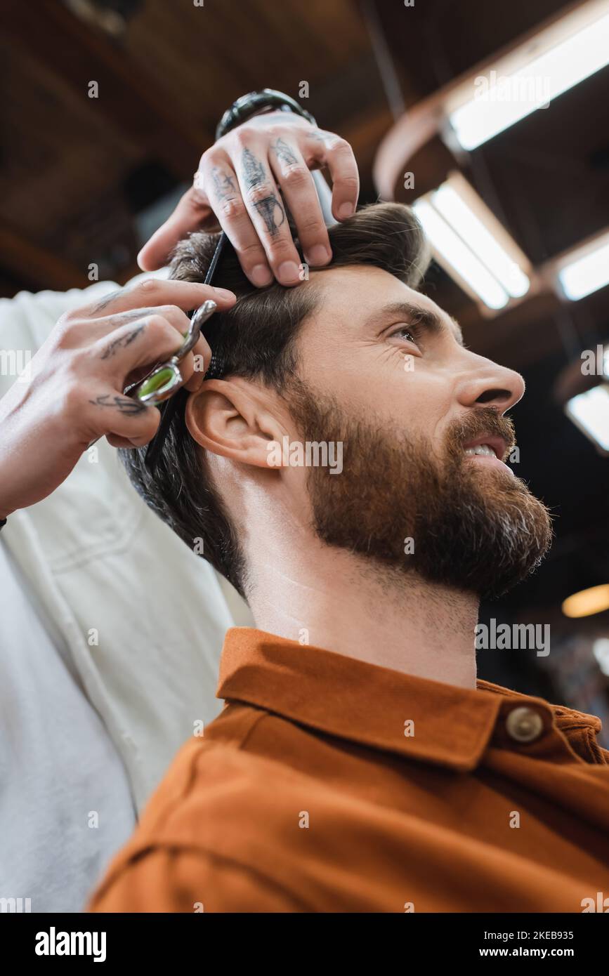 low angle view of hairstylist cutting hair of bearded smiling man,stock image Stock Photo