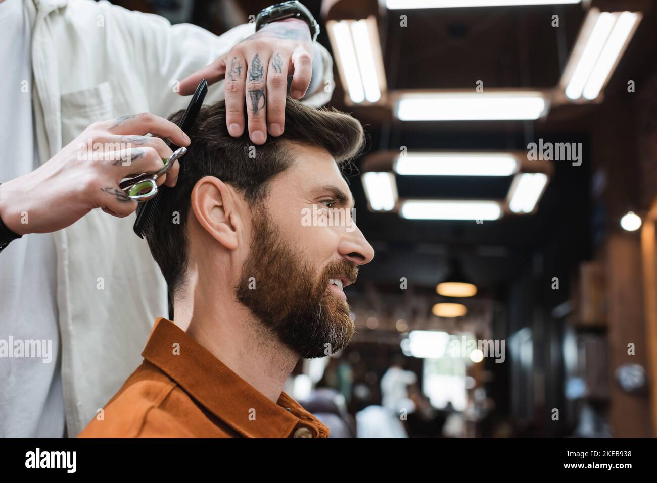 hairdresser cutting hair of brunette bearded man smiling in barbershop,stock image Stock Photo
