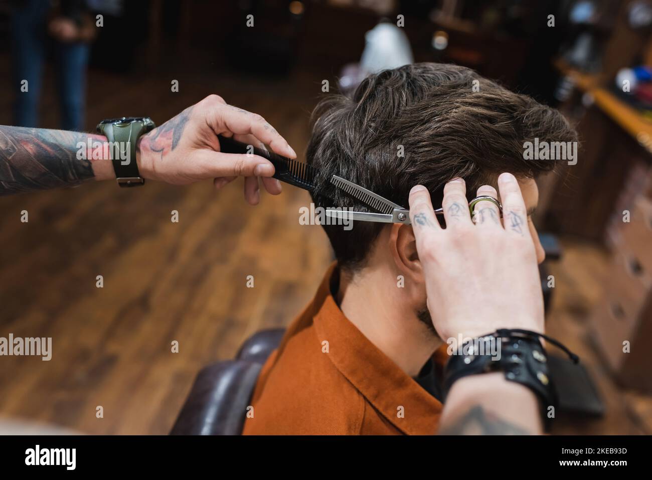 tattooed barber cutting hair of brunette man with thinning scissors,stock image Stock Photo