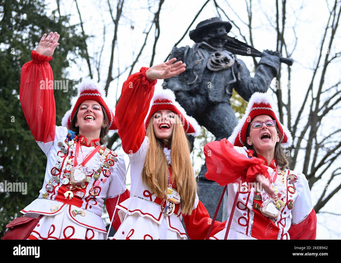 Hessen, Frankfurt/Main: 11 November 2022,  Lisa Retsch (l-r), Cyana Stojanovic and Anne-Lena Retsch from the KTC Rot-Weiß 1977 e.V. celebrate the return of their carnival symbol, the Urnarren, on 11.11 on H.P.-Müller-Platz in the Frankfurt district of Heddernheim, colloquially known as 'Klaa Paris'. The Urnarr is a gift from Lurgi AG for the 150th year of the Klaa Paris carnival and has stood at the subway station since 1989. It was dismantled a few weeks ago for repair and cleaning. Photo: Arne Dedert/dpa Stock Photo