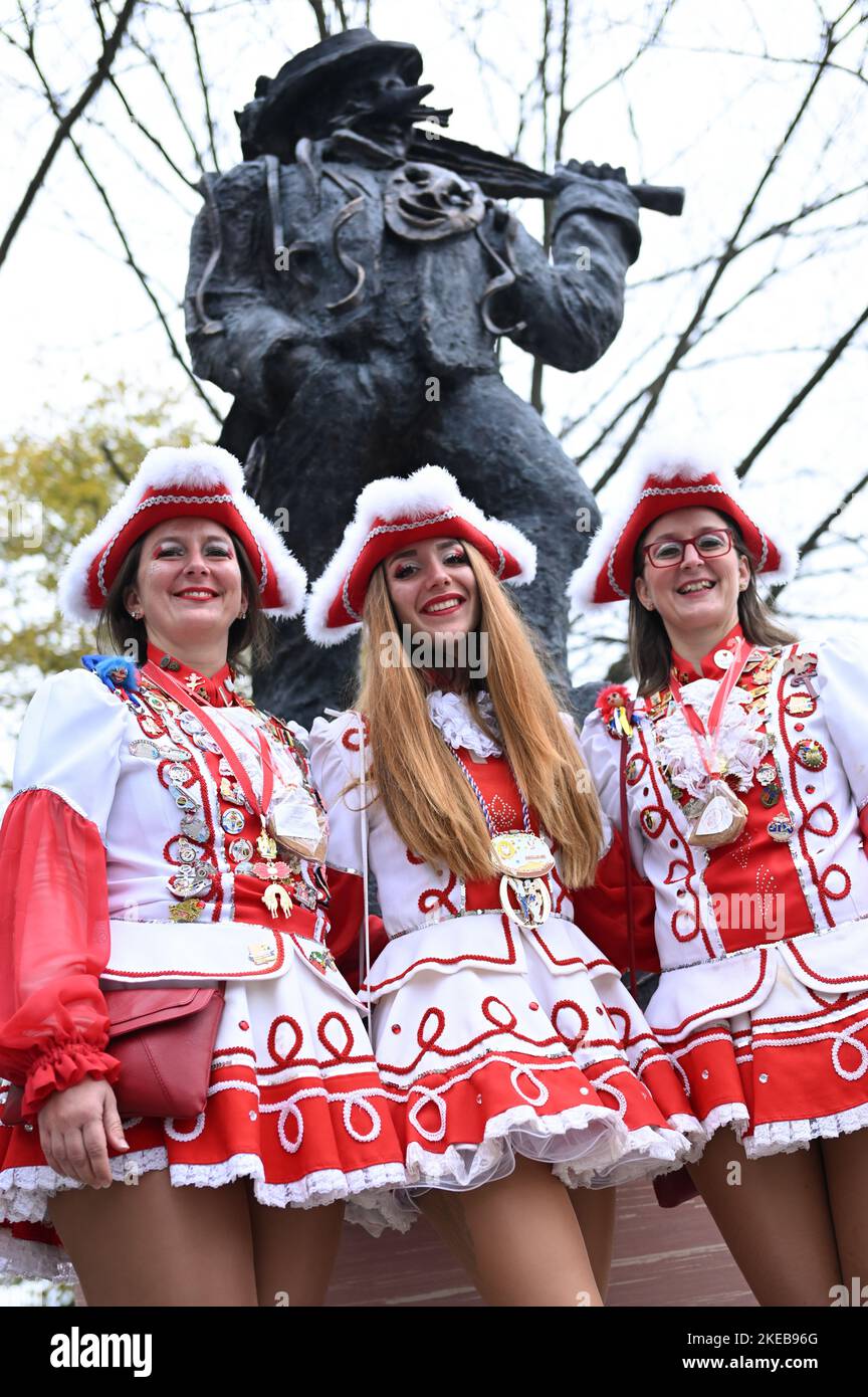 Hessen, Frankfurt/Main: 11 November 2022,  Lisa Retsch (l-r), Cyana Stojanovic and Anne-Lena Retsch from the KTC Rot-Weiß 1977 e.V. celebrate the return of their carnival symbol, the Urnarren, on 11.11 on H.P.-Müller-Platz in the Frankfurt district of Heddernheim, colloquially known as 'Klaa Paris'. The Urnarr is a gift from Lurgi AG for the 150th year of the Klaa Paris carnival and has stood at the subway station since 1989. It was dismantled a few weeks ago for repair and cleaning. Photo: Arne Dedert/dpa Stock Photo