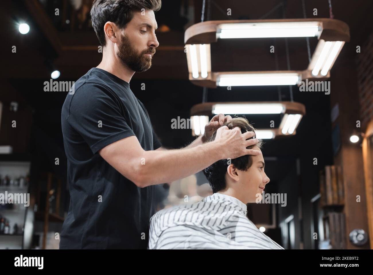 Side view of barber styling hair of teenager in cape in barbershop,stock image Stock Photo