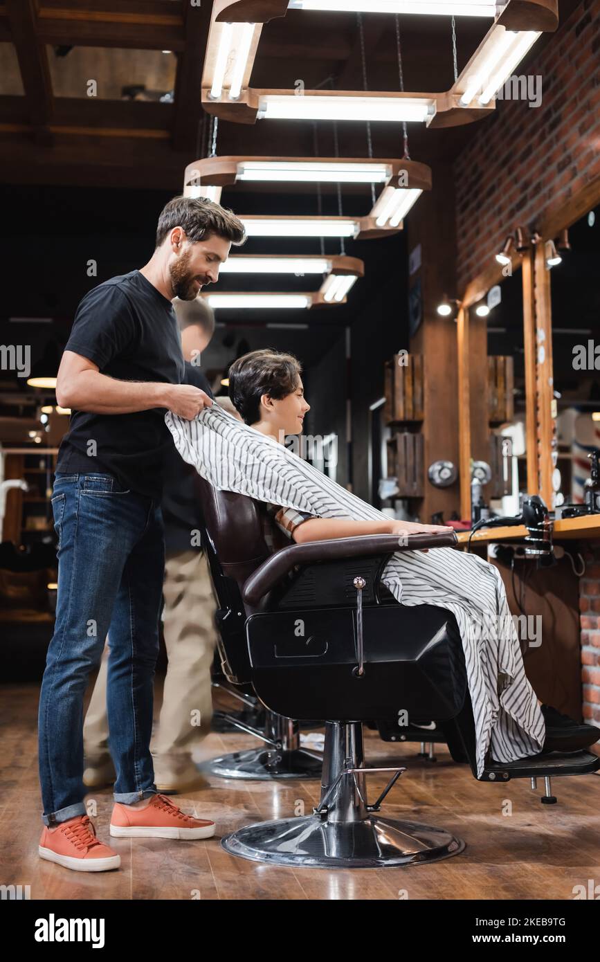 Side view of hairstylist taking off cape from teen customer in beauty salon,stock image Stock Photo