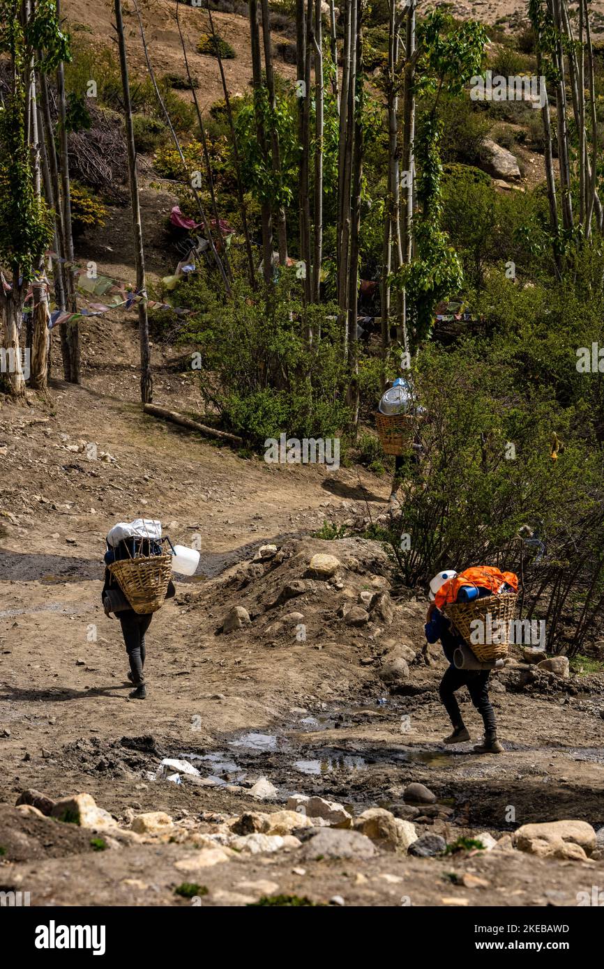 A vertical shot of two local Tibetan Buddhists carrying loads in Upper Mustang, Nepal Stock Photo