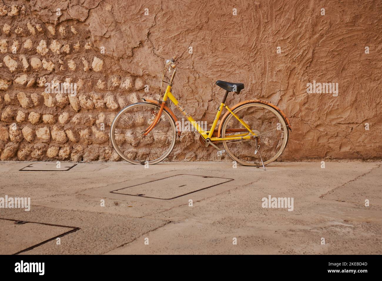 An old Bicycle or bike kept leaning beside earthen wall at Al Seef, Dubai Stock Photo