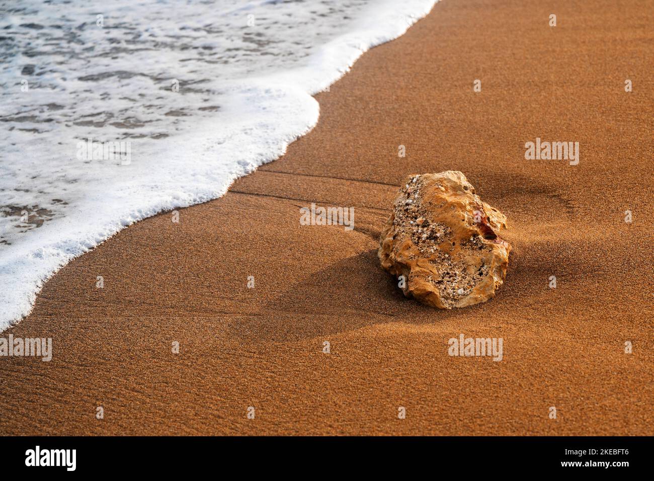 Small stone on sand beach with frothy sea aqua, nice texture of tiny grain of sand. Stock Photo
