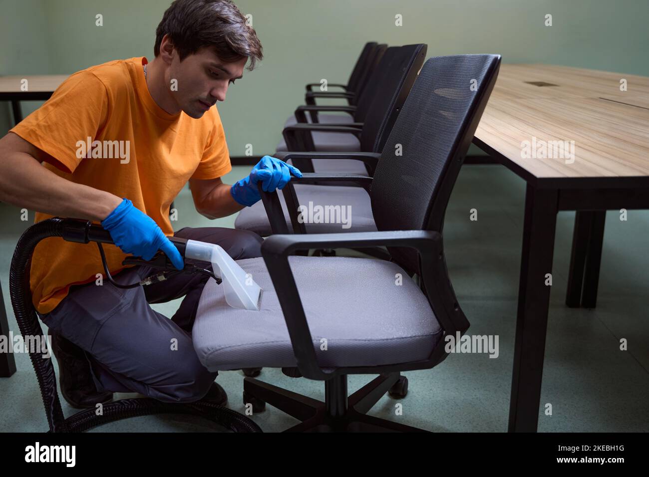 Hard-working janitor is deep-cleansing chairs with vacuum-cleaner Stock Photo